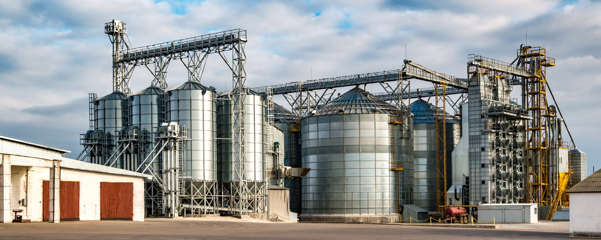 Plant with silos of different sizes in a yard in front of a cloudy sky